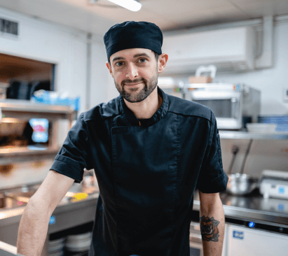 Image of chef at the pass serving up a dish